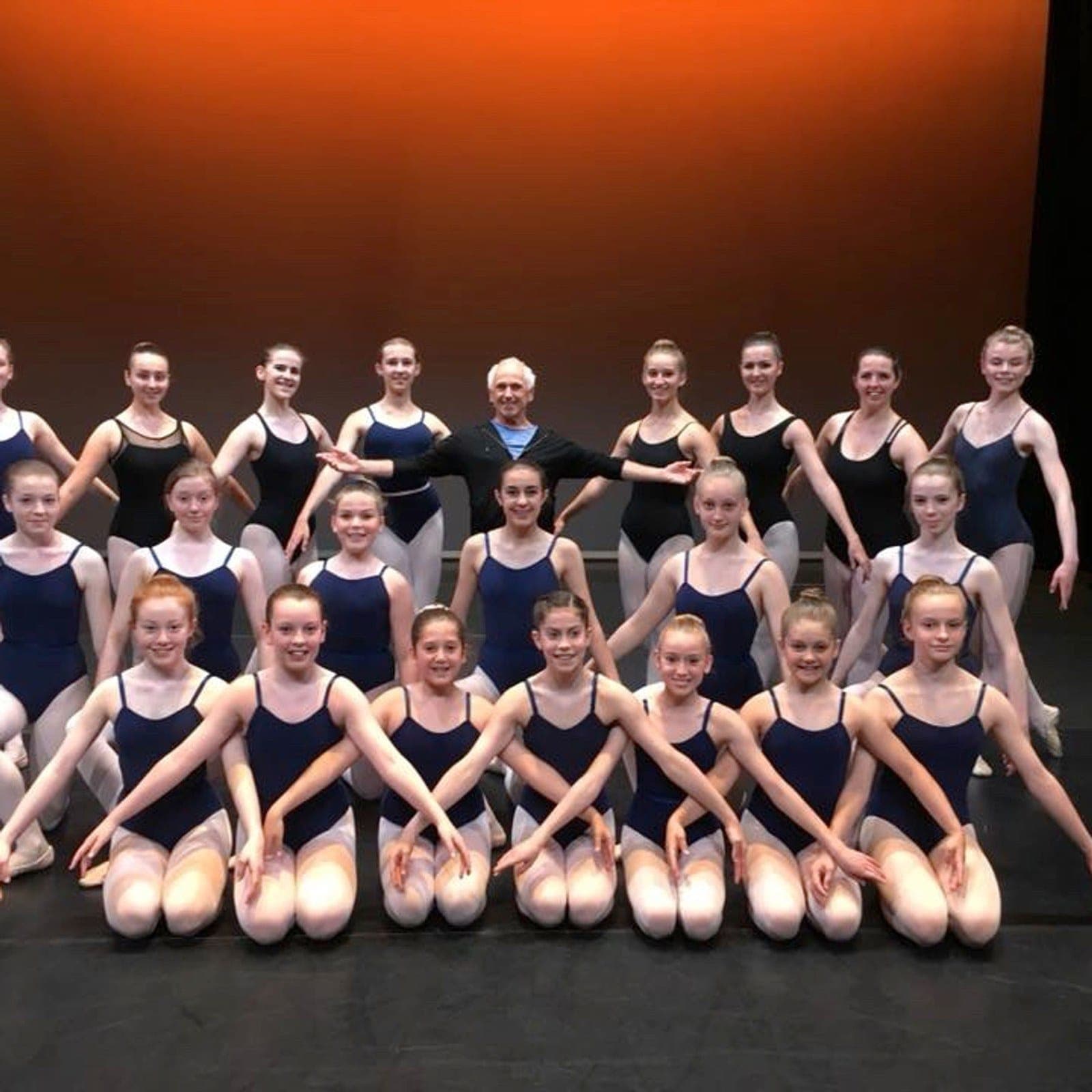 Ballet company in navy leotards posed with their teacher